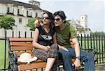 Young couple sitting on a bench and a cathedral in the background Se Cathedral, Goa, India