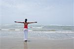 Rear view of a young woman standing on the beach with her arms outstretched