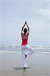 Rear view of a young woman standing in a tree pose on the beach