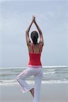 Rear view of a young woman standing in a tree pose on the beach