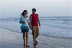 Young man walking on the beach with a young woman holding a glass of drink