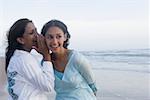 Side profile of a young woman whispering into her friend's ear on the beach
