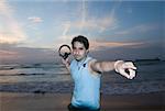 Portrait of a young man holding headphones and pointing on the beach