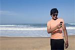 Young man standing on the beach and text messaging