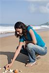 Seitenansicht einer jungen Frau spielen mit Muscheln am Strand