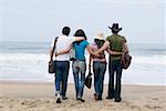 Vue arrière de deux jeunes couples marchant sur la plage avec leurs bras autour de l'autre