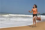 Junge Frau am Strand laufen und halten eine Handtasche