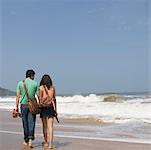 Vue arrière d'un jeune couple tenant leurs pantoufles et marchant sur la plage