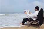 Jeune homme lisant un journal sur la plage