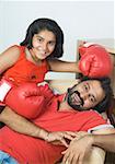 Portrait of a mid adult man reclining on a couch with his daughter wearing boxing gloves