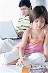 Nahaufnahme von einem Mädchen mit ihrem Vater arbeitet an einem Laptop hinter ihr eine Magazin lesen