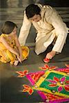 Mid adult man making a rangoli with his daughter