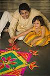 High angle view of a mid adult man making rangoli with his daughter