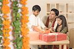 Young man sitting with his children and opening diwali gifts