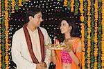 Young woman holding a diwali thali with a young man standing beside her