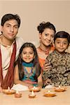 Portrait of a young couple sitting together with their son and daughter behind diwali lamps