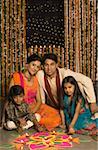 Portrait of a young couple with their son and daughter sitting behind a rangoli