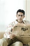 Mid adult man sitting on a couch and reading a newspaper