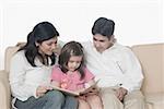 Mid adult couple with their daughter sitting on a couch and reading a book