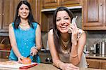 Young woman talking on a cordless phone with her mother cutting tomato behind her