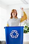 Frau wirft Papier in Recyclingbehälter