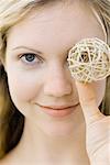 Young woman holding ball in front of one eye, smiling at camera, portrait