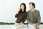 Couple sitting side by side, woman using cell phone, man wearing headset, both smiling