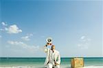 Man sitting next to suitcase at the beach, shouting into megaphone