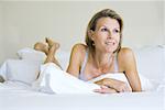 Woman lying on stomach on bed, looking away, smiling