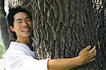 Homme hugging tronc d'arbre, souriant à la caméra