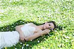 Young woman lying in meadow, touching flowers, looking away