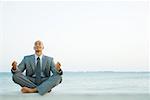 Businessman sitting in lotus position at the beach, eyes closed