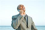 Businessman at the beach using cell phone, laughing, eyes closed