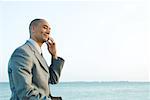 Businessman by the sea using cell phone, smiling, side view