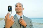 Businessman photographing self with cell phone at the beach, smiling, adjusting tie