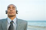 Businessman listening to headphones at the beach, eyes closed, close-up