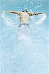 Man swimming and splashing in pool, rear view