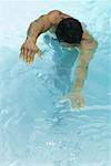Homme nageant dans la piscine, bras tendus, tête vers le bas