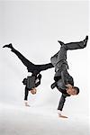 two business men doing handstand with one hand