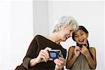 Senior woman photographing self and daughter with digital camera, both laughing