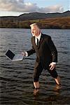 Businessman Walking through Lake with Laptop Computer