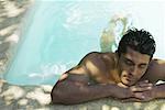 Man holding on to edge of swimming pool, head resting on arms, eyes closed