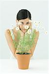 Woman behind potted chamomile, holding head, smiling at camera, portrait