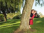 Young boy and girl hiding behind tree