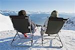 Man, woman relax on deck chairs in snow