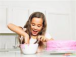 Girl (8-10) dipping finger in icing bowl