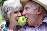 Senior couple both biting apple