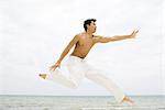 Man leaping in the air, side view, ocean in background