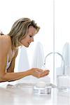 Woman leaning over bathroom sink, holding hands under running water