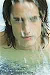 Man in swimming pool, looking at camera through splashing water